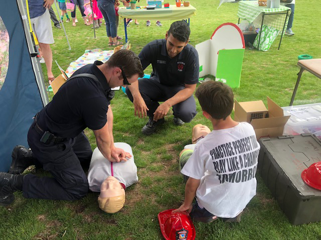 Firefighters demonstrating CPR while a local youth watches.